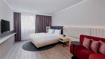 A hotel room with a bed, a TV, a red sofa, and a small table.