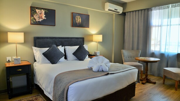 Een netjes ingerichte hotelkamer met een groot bed, twee nachtkastjes met lampen, een klein rond tafeltje en een stoel.