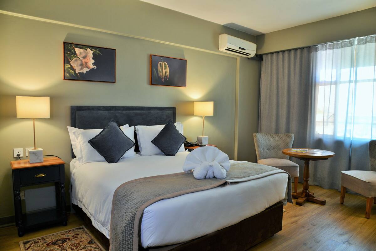 A neatly arranged hotel room with a large bed, two bedside tables with lamps, a small round table, and a chair.
