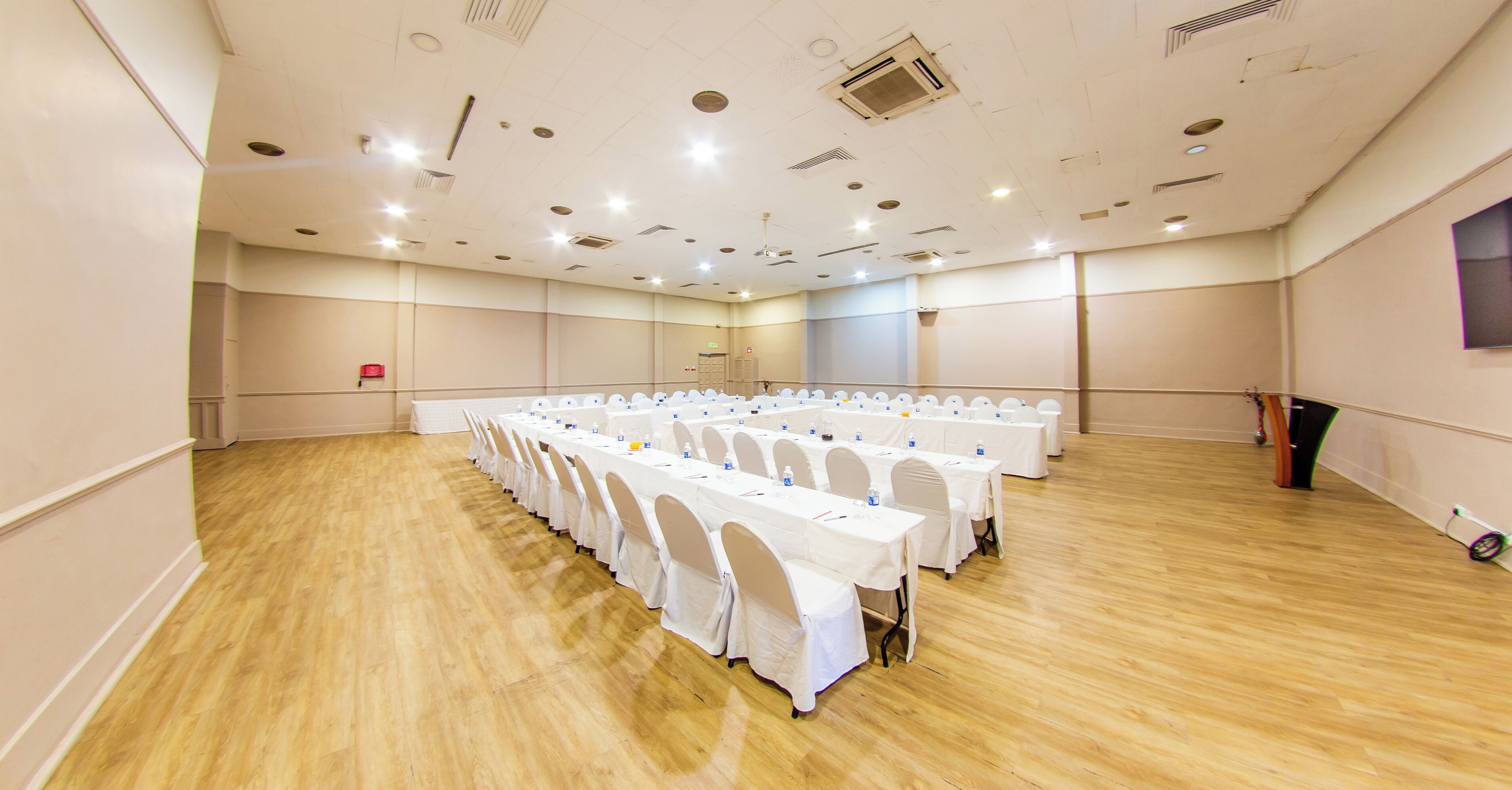 A large conference room with multiple tables and chairs, a wooden floor, and a high ceiling with recessed lighting.