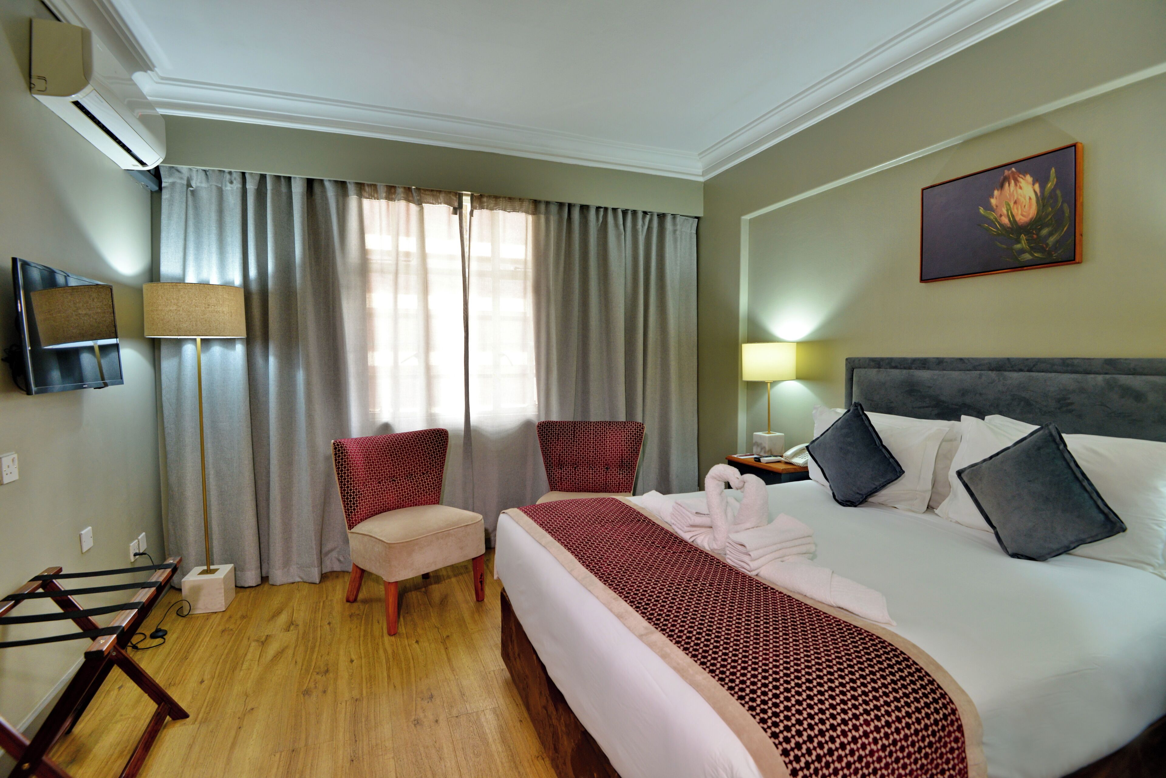 Ein Hotelzimmer mit einem Bett, zwei Stühlen, einem Fernseher und einem Gemälde an der Wand.
