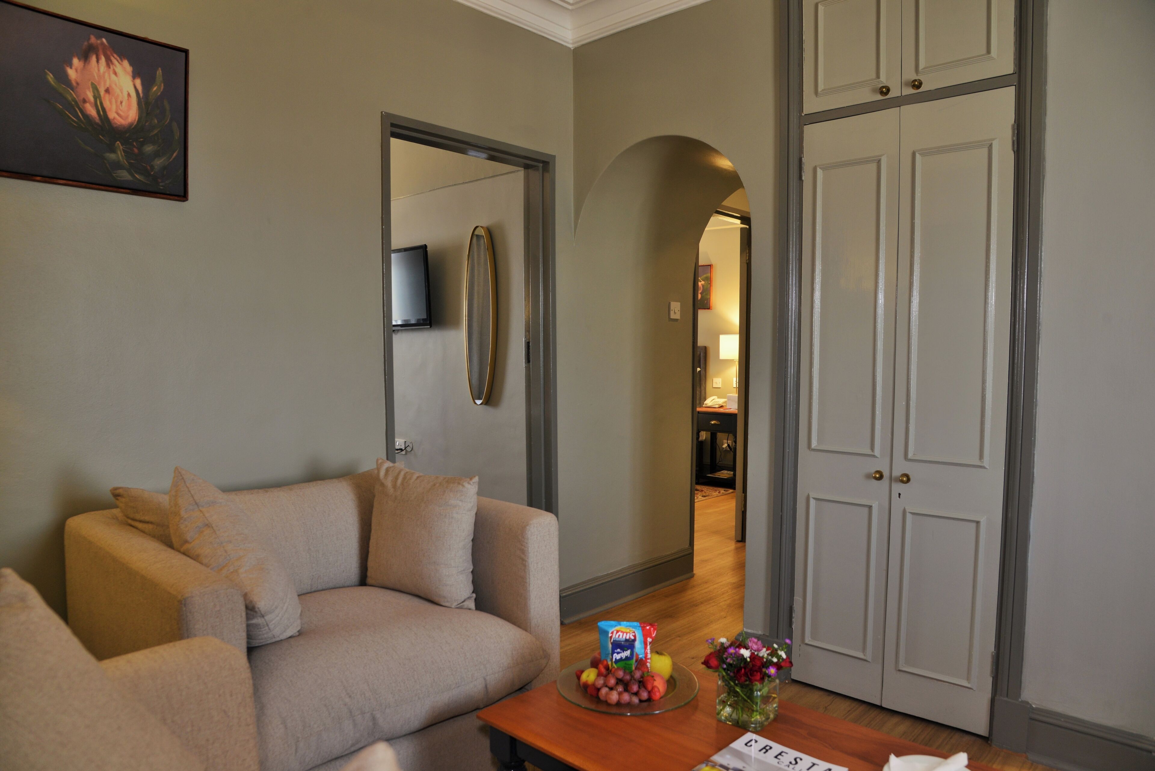 A living room with a sofa, a coffee table with snacks and flowers, a TV, and a door leading to another room.