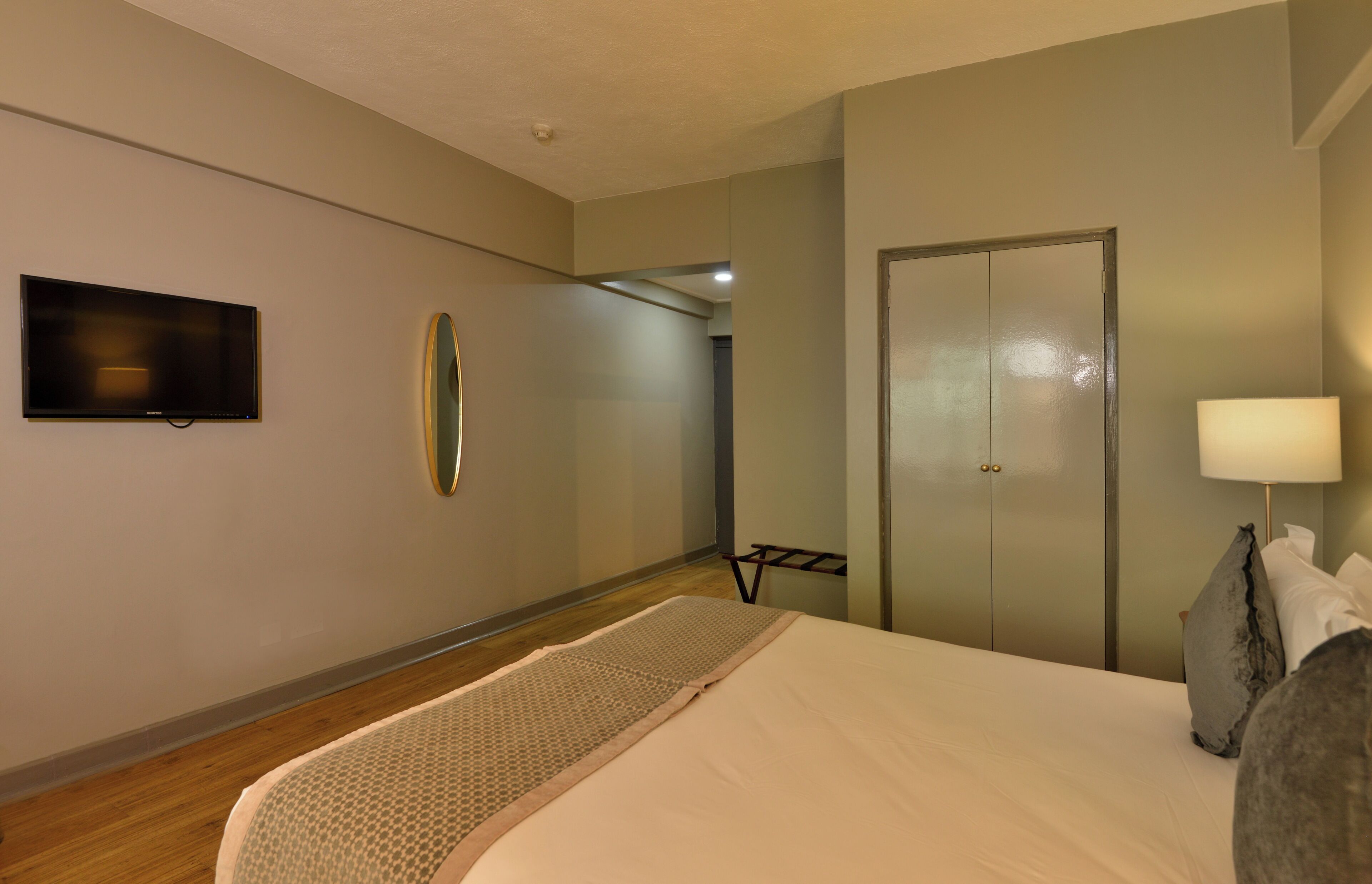 Habitación de hotel con cama, televisor de pantalla plana, puerta, lámpara y una mesita.