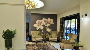 Een goed verlichte woonkamer met een grote bloemenmuur, twee fauteuils, een salontafel en een bijzettafeltje met een plant.