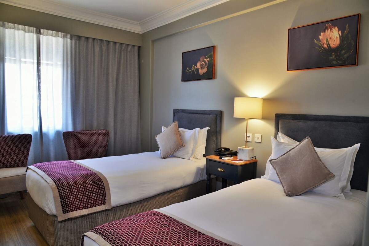 Une chambre d’hôtel avec deux lits, une table de chevet, une lampe et un tableau au mur.