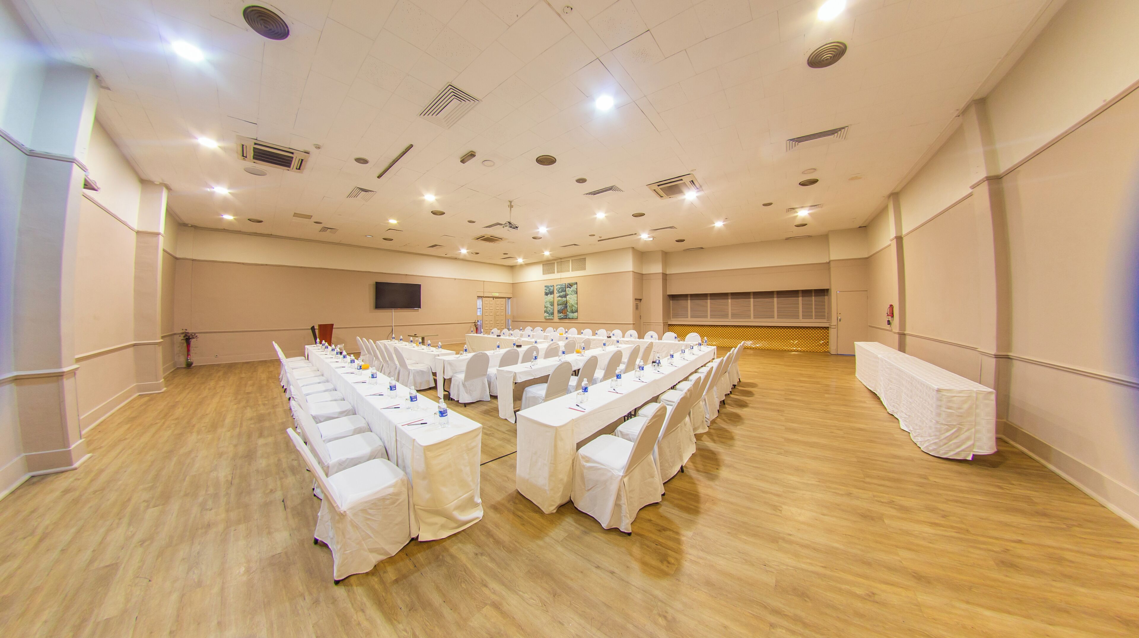 Una sala conferenze con file di tavoli, tovaglie bianche e sedie, dotata di bottiglie d'acqua e penne.