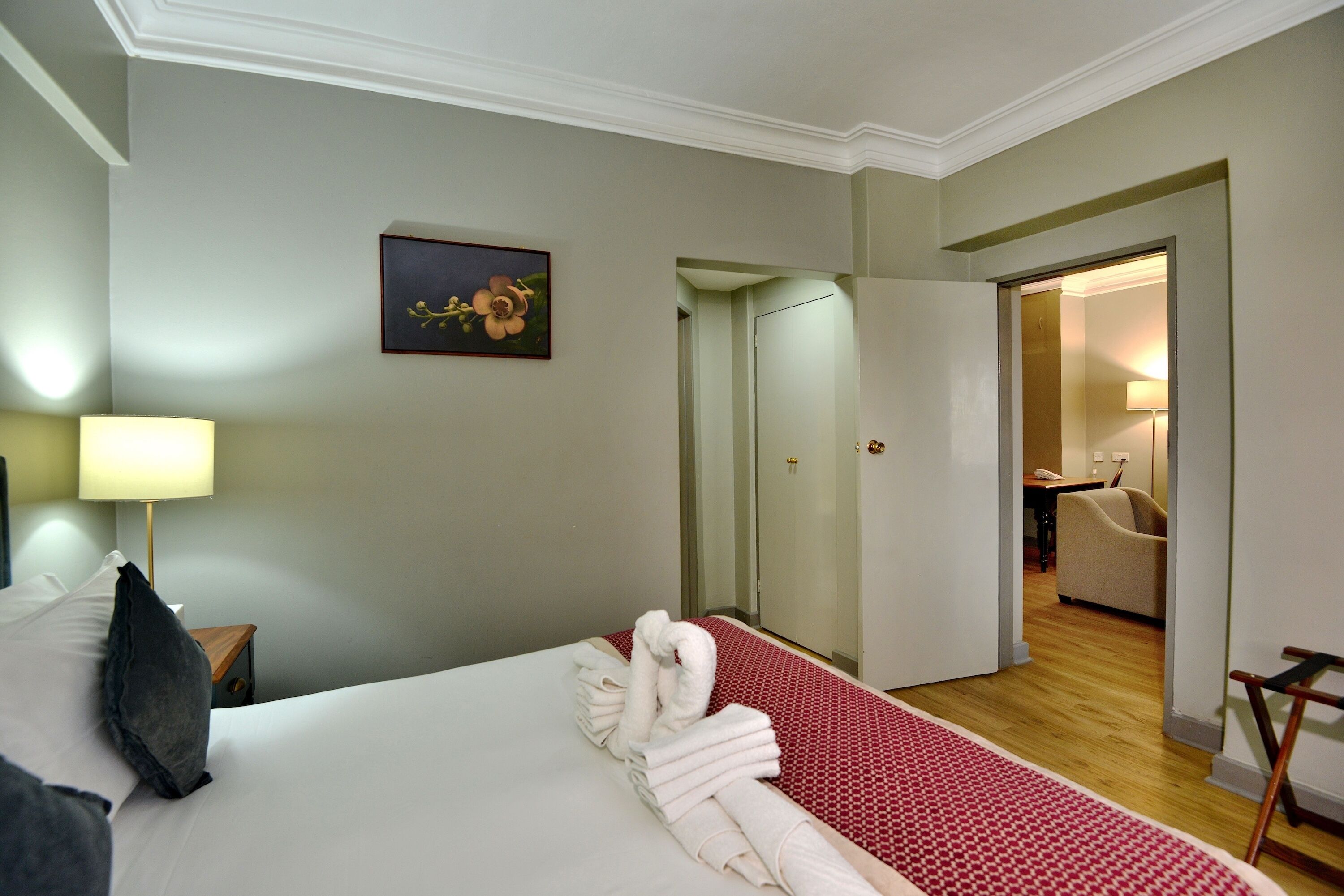 Una habitación de hotel con una cama bien hecha, un cuadro en la pared y vistas a la habitación contigua.