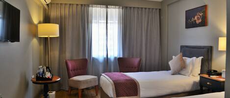 Ett hotellrum med två sängar, ett skrivbord med en lampa, en stol och en tavla på väggen.