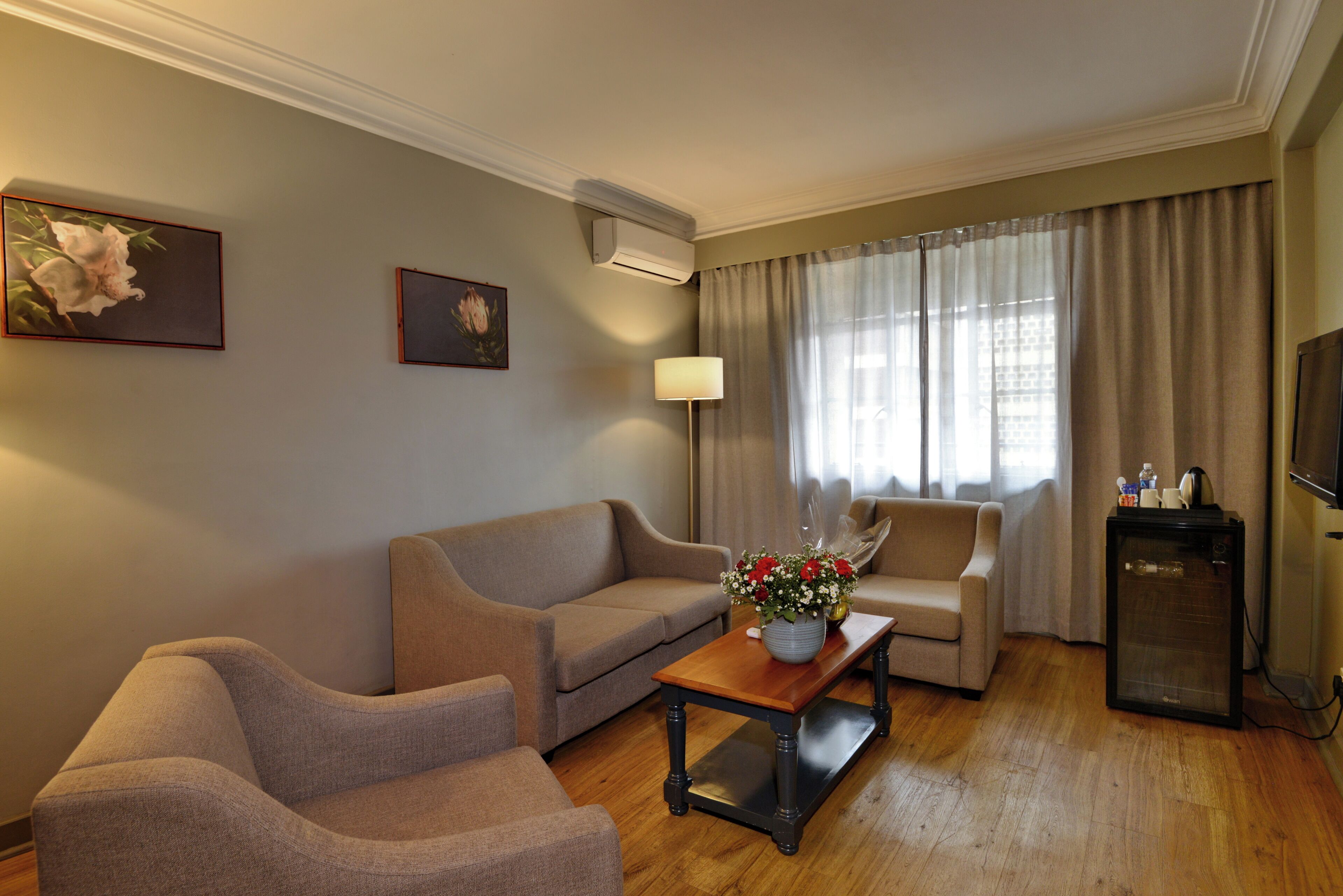 A living room with a sofa, armchair, a coffee table with a vase, a lamp, and a television.