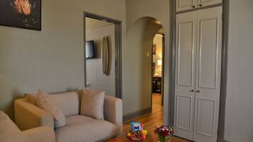 Un salón con un sofá beige, una mesa de centro con aperitivos y un jarrón de flores, y un televisor en la pared.
