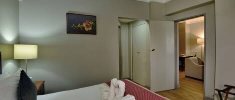 A hotel room with a neatly made bed, a painting on the wall, and a door leading to a bathroom.