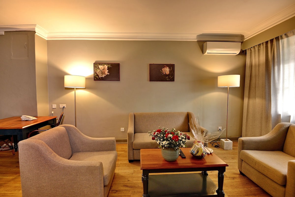 A living room with a sofa, armchairs, a coffee table with a vase of flowers, and two wall-mounted lamps.