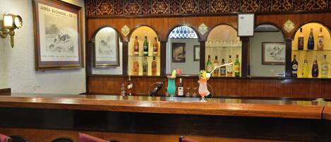 Zona de bar amb taulell de fusta, cadires tapissades de vermell i diverses ampolles de licors.