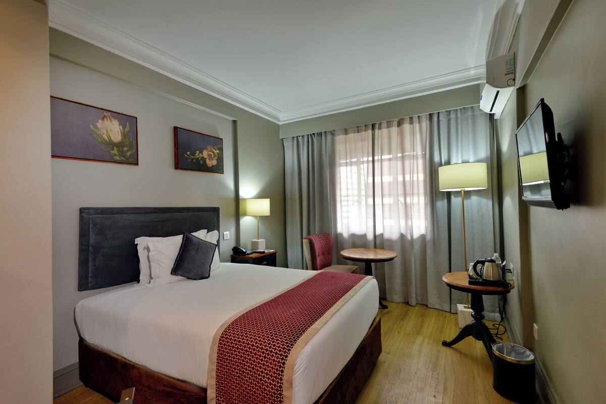 A hotel room with a bed, a desk, a chair, a TV, and a window with curtains.