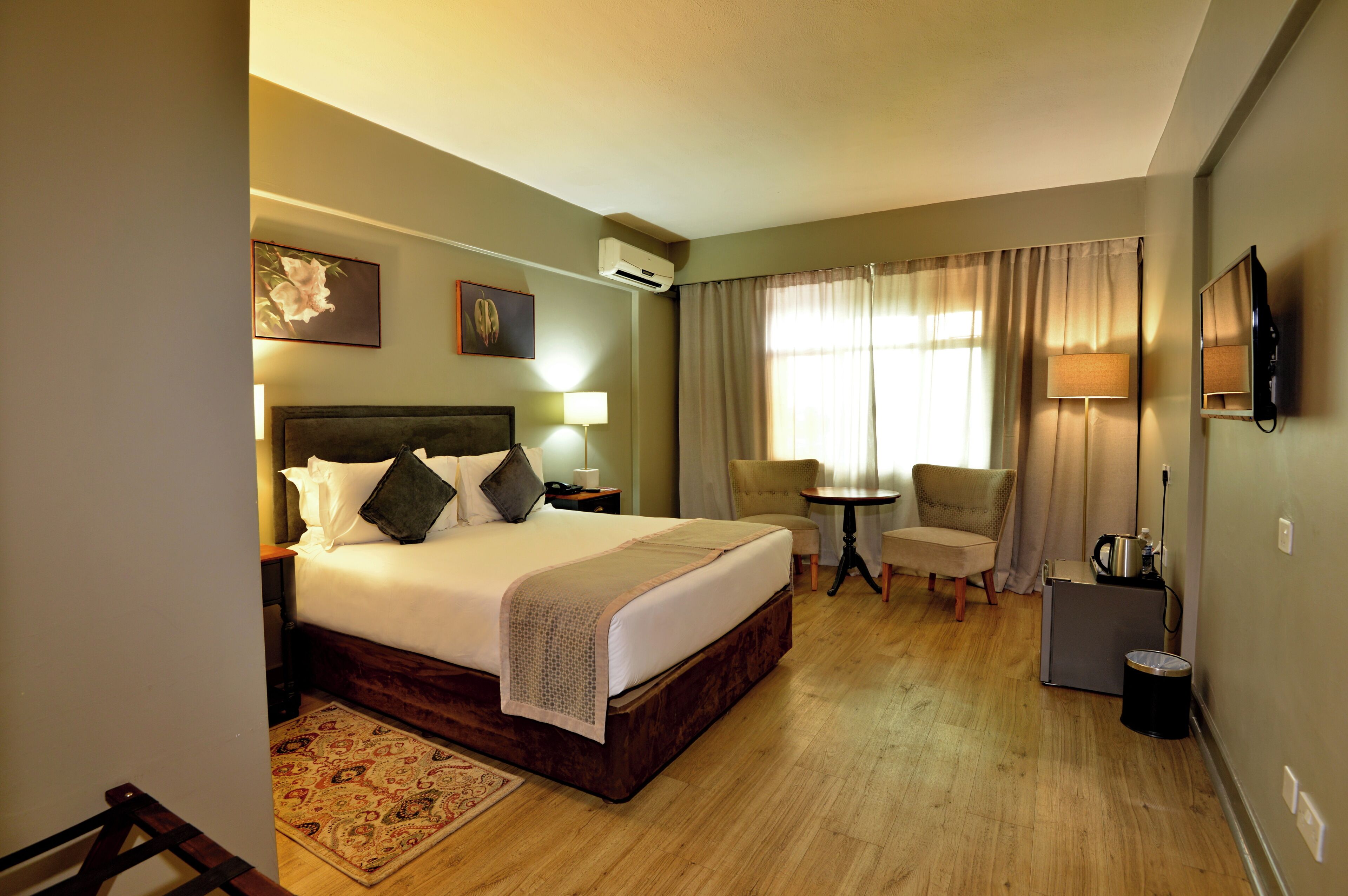 Ein Hotelzimmer mit einem großen Bett, einem Schreibtisch, einem Sessel, einem Fernseher und einem Fenster mit Vorhängen.
