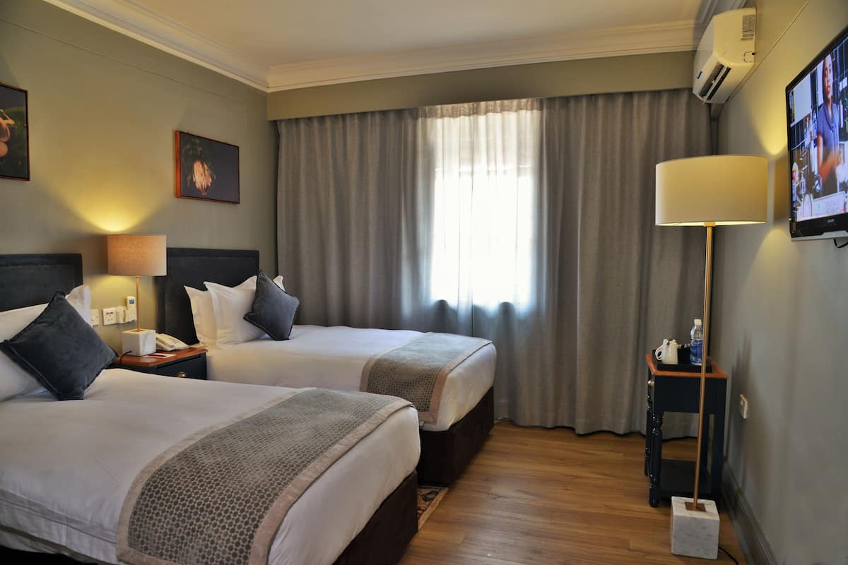 A hotel room with two beds, a TV, a lamp, and a small table with a water bottle.