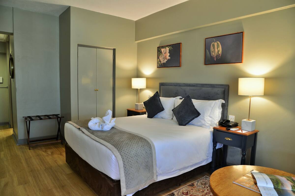 A hotel room with a bed, bedside lamps, a nightstand, a wooden side table, and a door.