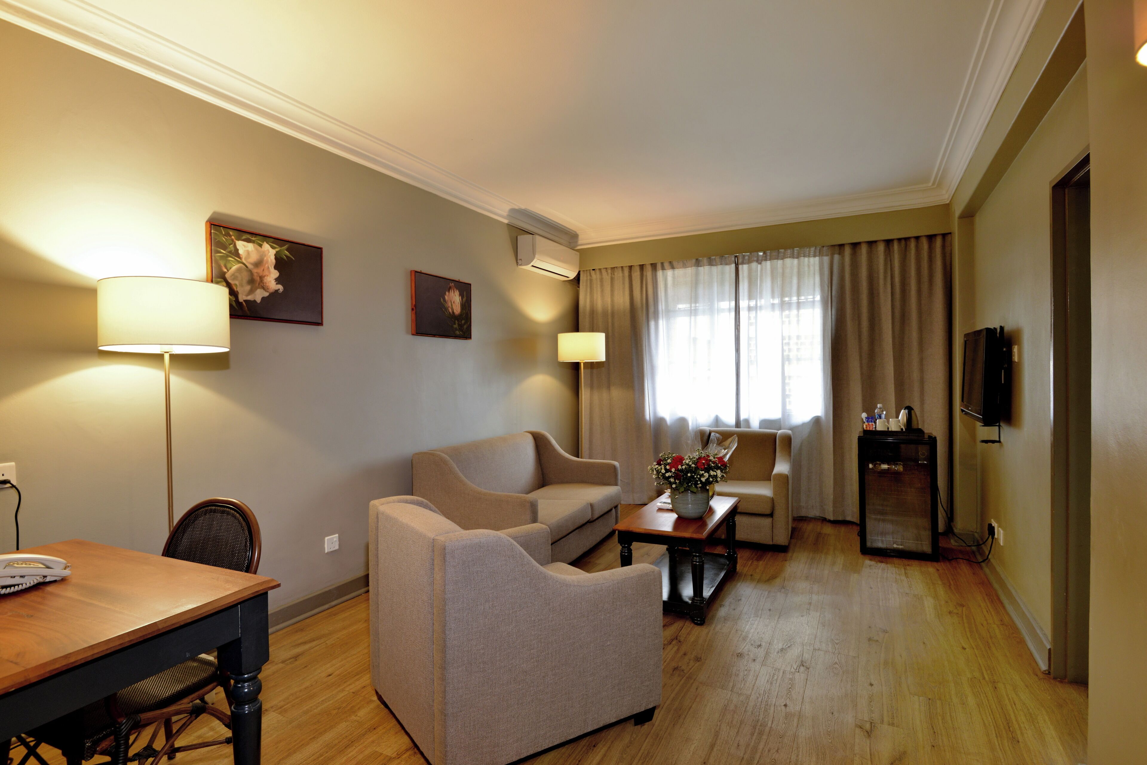 A hotel room with a sofa, a dining table, a coffee table, a TV, and a window with curtains.
