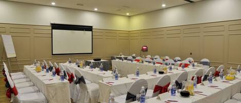 A conference room with multiple tables, chairs, and a projector screen.