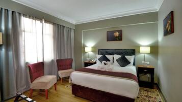 Una habitación de hotel con cama, dos sillas, una mesita de noche, una lámpara y un cuadro en la pared.