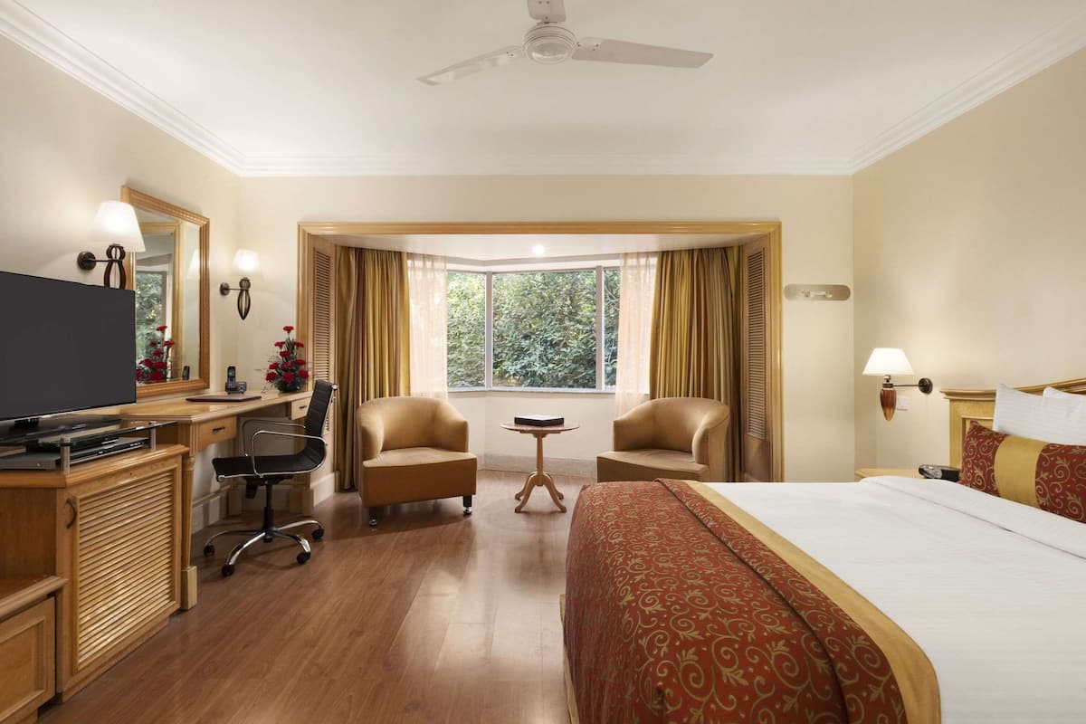 Une chambre d’hôtel équipée d’un lit, d’un bureau, de chaises, d’une télévision et d’une fenêtre avec des rideaux.
