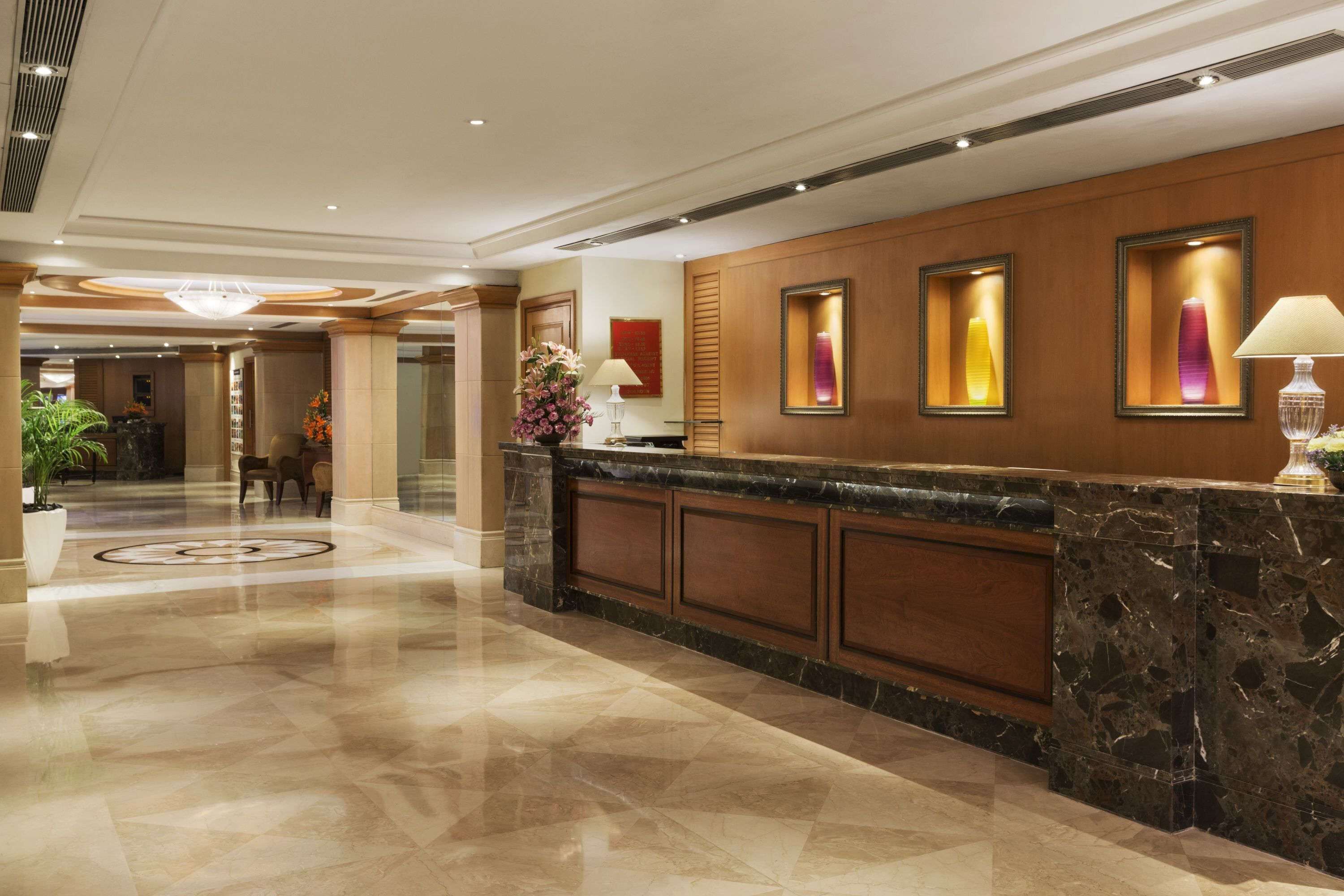 A hotel reception area with a marble counter, framed artwork, and a potted plant.