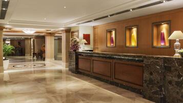 A hotel reception area with a marble counter, framed artwork, and a potted plant.