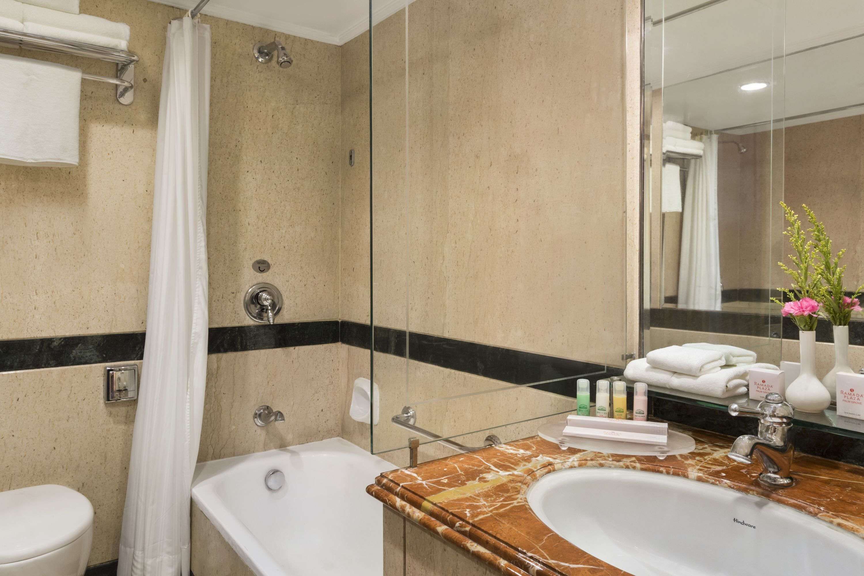 A bathroom with a bathtub, a sink, and a shower. There are toiletries on the counter, and towels are hanging on a rack.