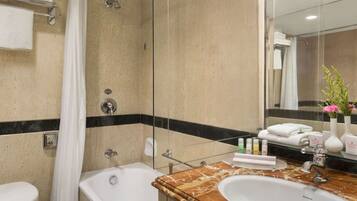 A bathroom with a bathtub, a sink, and a shower. There are toiletries on the counter, and towels are hanging on a rack.