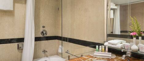 A bathroom with a bathtub, a sink, and a shower. There are toiletries on the counter, and towels are hanging on a rack.
