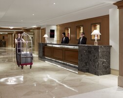 A hotel reception area with a marble counter, a luggage cart, and reception staff.