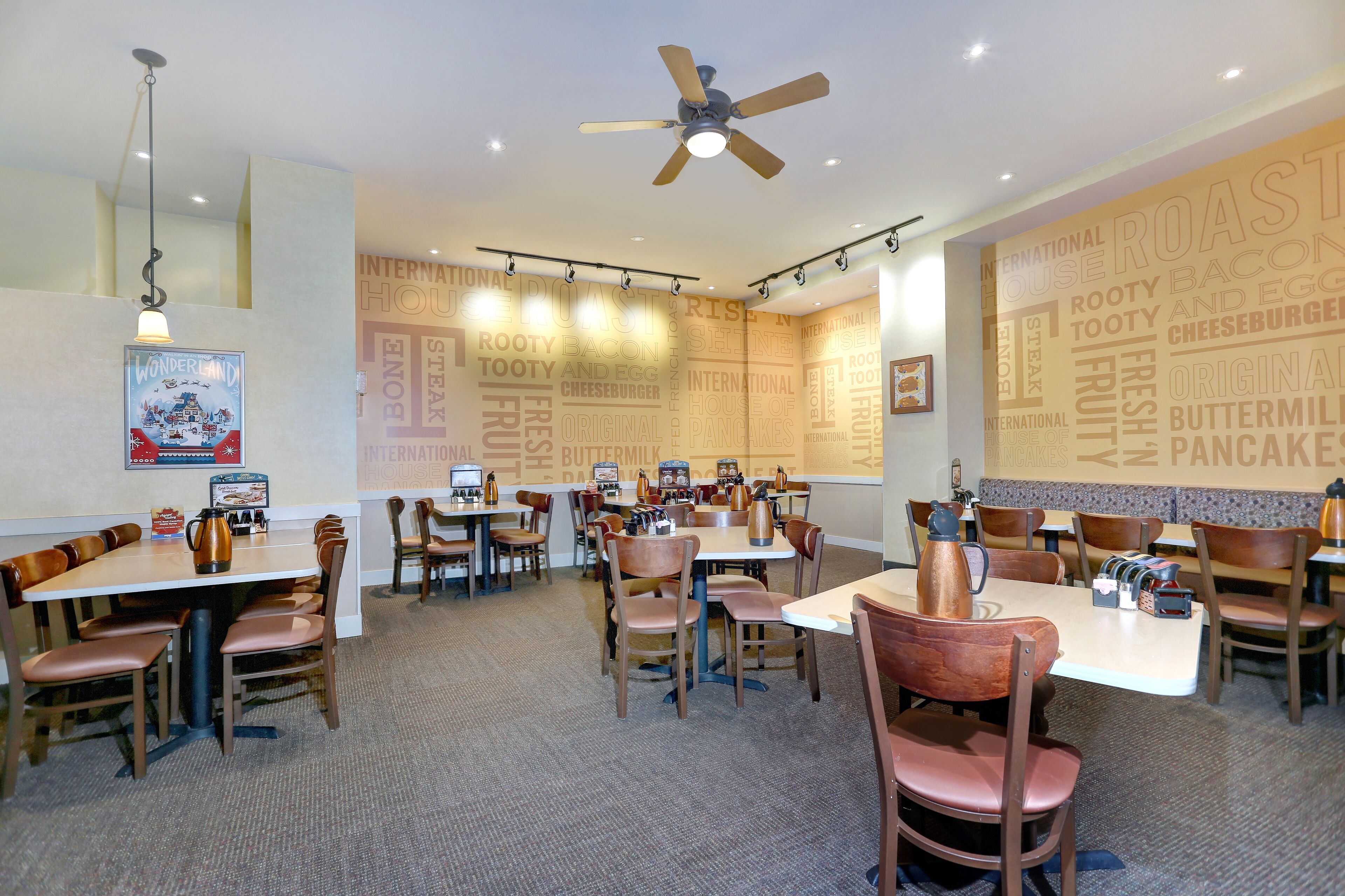 A restaurant with multiple tables and chairs, ceiling fans, and a wall with food-related words.