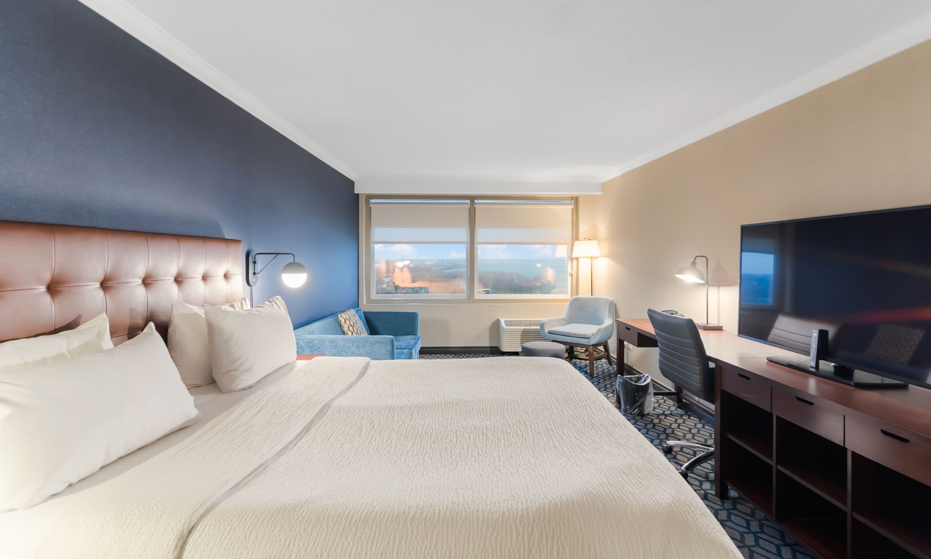 A hotel room with a large bed, a desk with a computer, a chair, and a TV.
