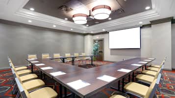 A conference room with a long table, chairs, a projector screen, and a carpeted floor.