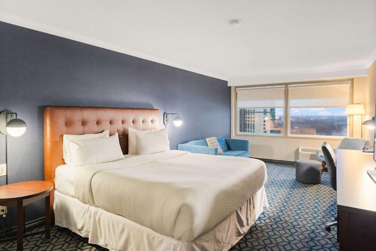 Habitación de hotel con una cama grande, un escritorio, una silla, un sofá y vista a la ciudad.