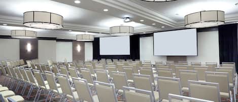 Une salle de conférence avec des rangées de chaises, un écran de projection et un grand écran.