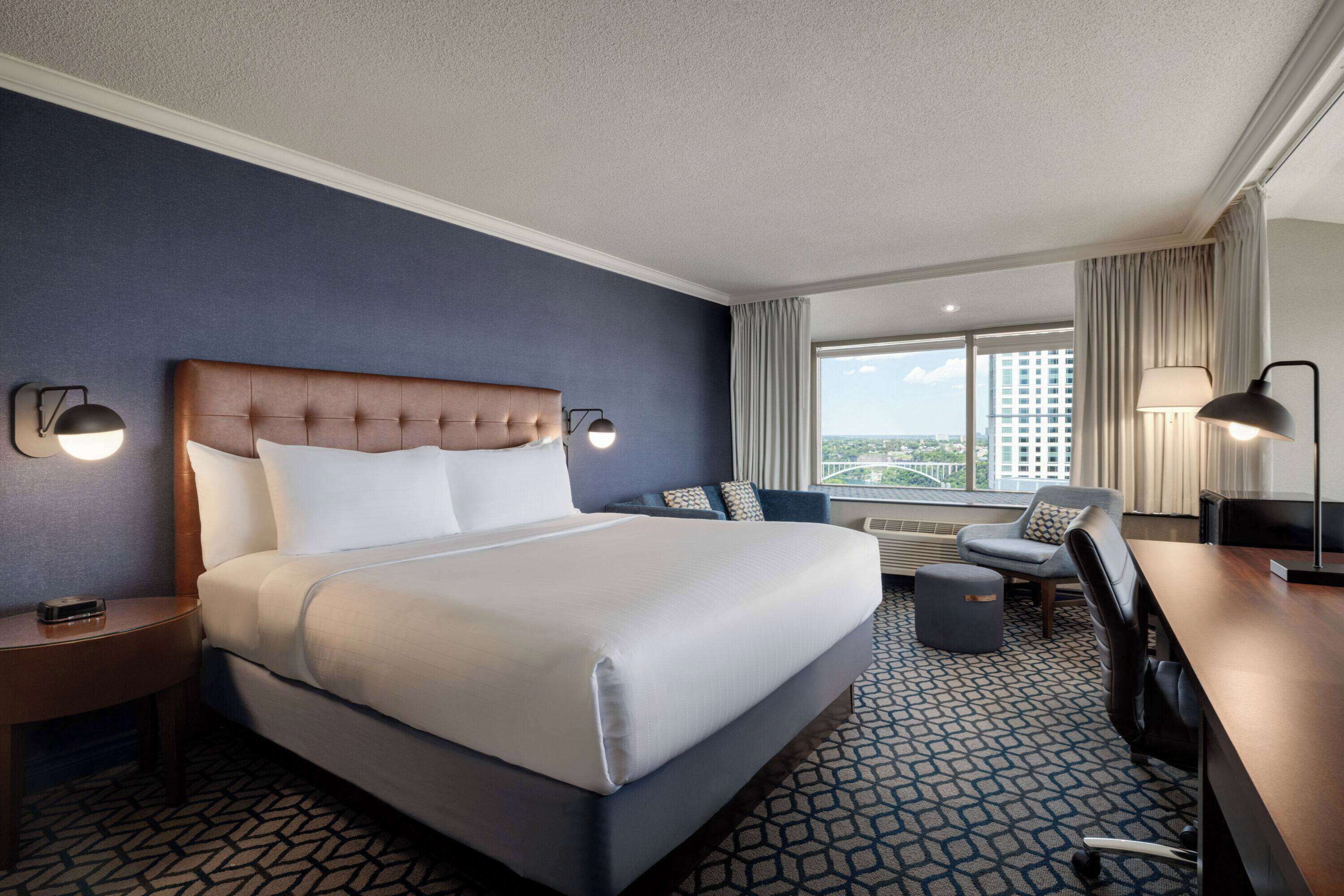 Habitación de hotel con una cama grande, un escritorio, una silla y vistas a la ciudad.