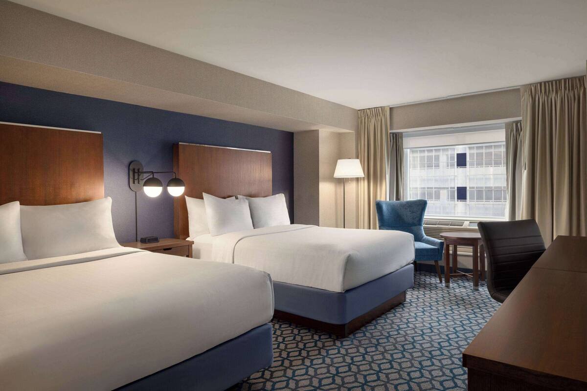 A hotel room with two beds, a desk, a chair, and a window with curtains.