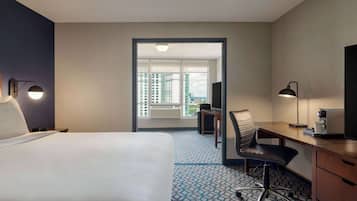 Habitación de hotel con cama, escritorio, silla y vistas a edificios a través de una puerta.