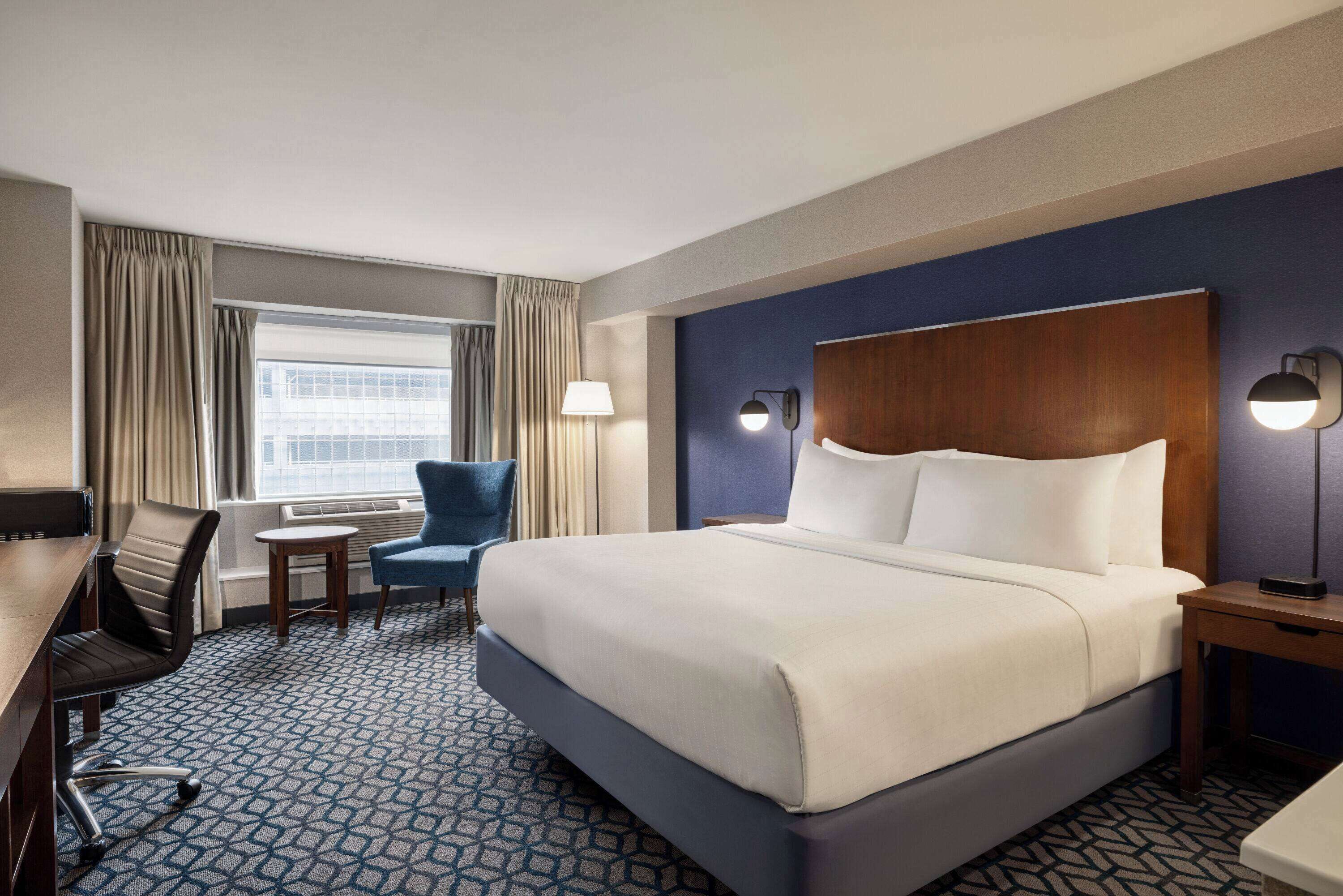 Habitación de hotel con una cama grande, un escritorio con silla, una mesita y una lámpara.