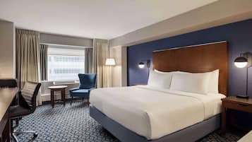 Habitación de hotel con una cama grande, un escritorio con silla, una mesita y una lámpara.