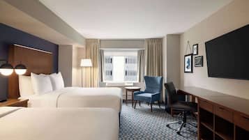 A hotel room with two beds, a desk, a chair, a TV, and a window with curtains.
