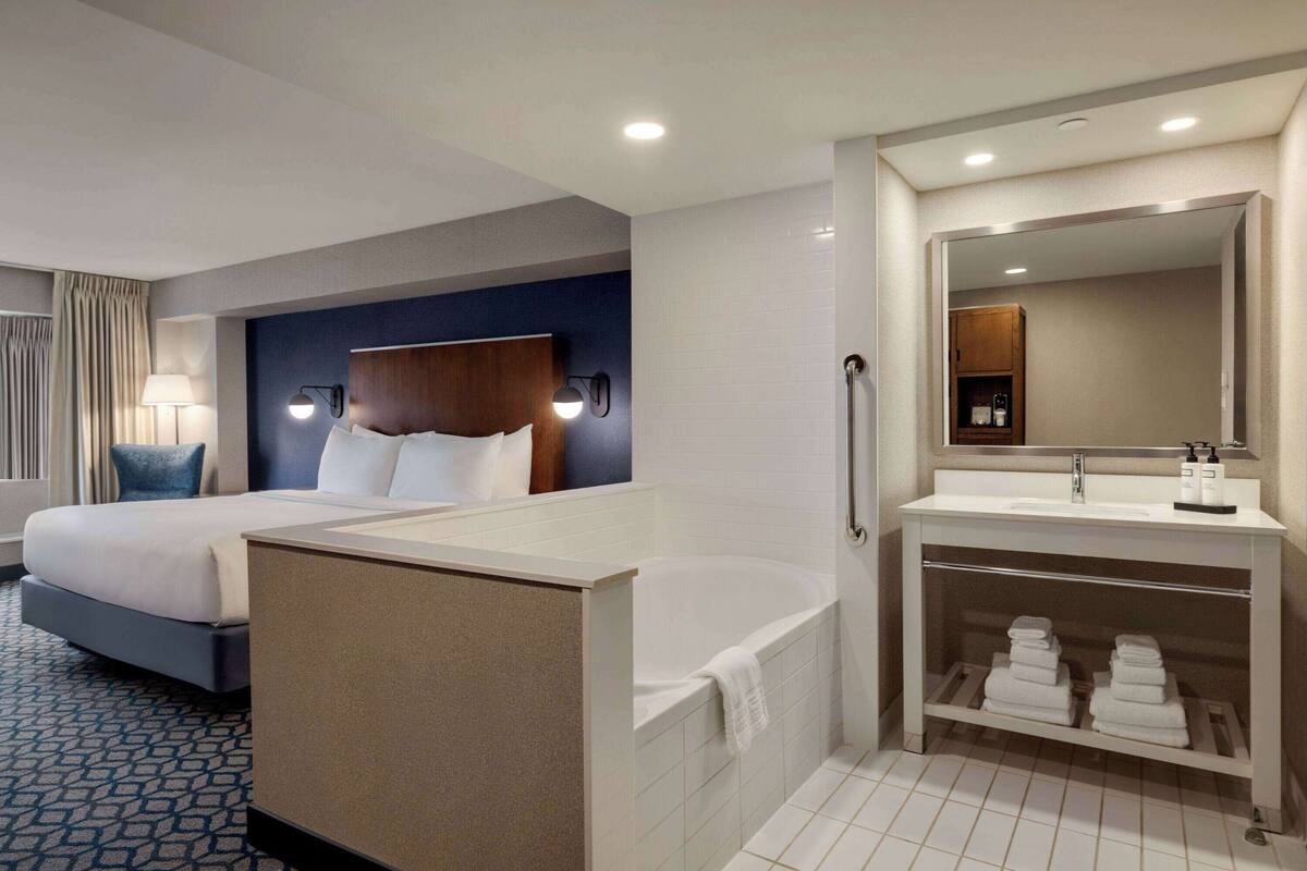 A hotel room with two beds, a large bathtub, a vanity with a mirror, and a towel rack.