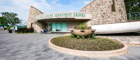 La façade extérieure du George Fore Discovery Center, avec son parement en pierre, un grand jardon au premier plan et un ciel bleu clair en arrière-plan.