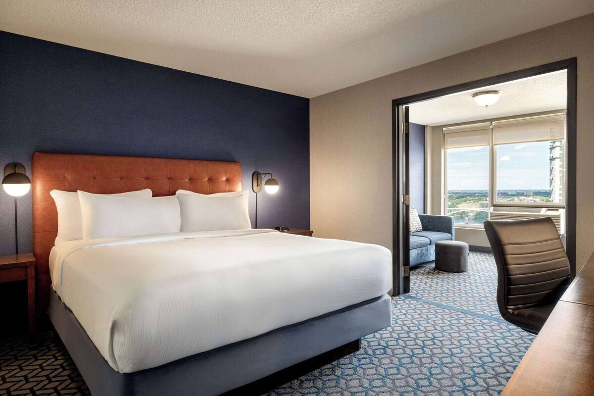 A hotel room with a large bed, a sofa, a desk, and a view of the city.