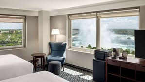 Une chambre d’hôtel avec deux lits, une chaise, un bureau avec une télévision et une vue sur une cascade.
