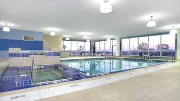 An indoor swimming pool with clear blue tiles, a sunlit room with large windows, and a view of the sunset.