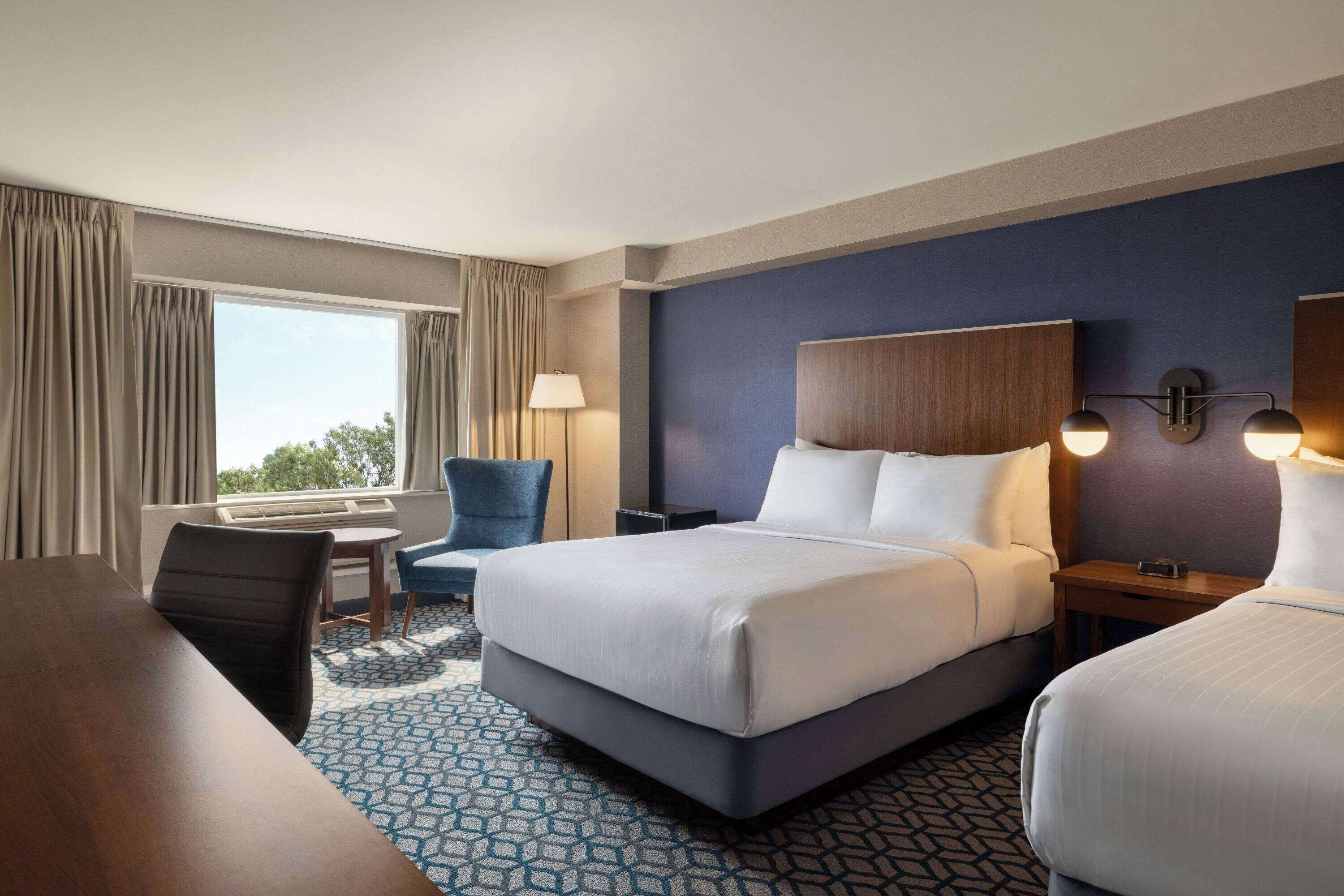 A hotel room with a large bed, a desk, a chair, and a window with curtains.