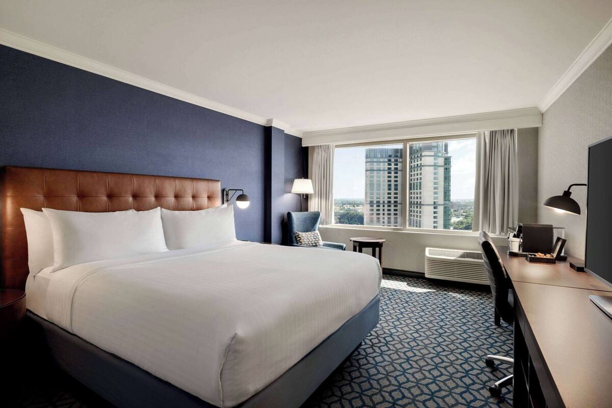 A hotel room with a large bed, a desk, a chair, and a window with a city view.