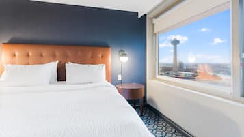 Une chambre d’hôtel avec un grand lit, une petite table ronde, une lampe fixée au mur et une fenêtre donnant sur le paysage urbain.
